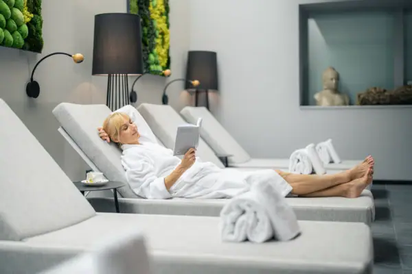 Wellness Louis C. Jacob Hamburg A woman lying on a lounge chair reading a book indoors.