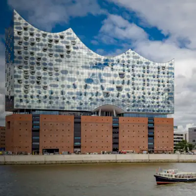 Elbphilharmonie A boat on the water next to a building under a cloudy sky.