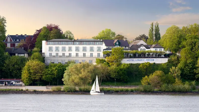 Louis C. Jacob Hotel Hamburg White building with a sailboat on a body of water.