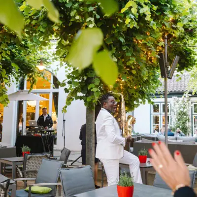 Events on the Linden Terrace A man in a white suit is playing the saxophone under a tree.